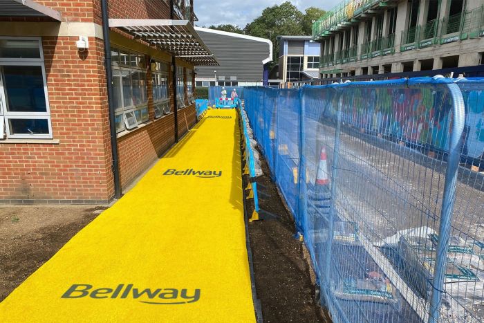 Yellow spaghetti site mat forming a branded pedestrian walkway on a Bellway construction site