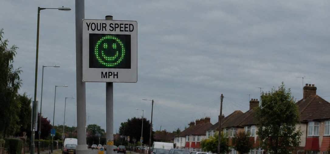 Vehicle activated sign at site entrance showing green smiley face on UK residential road
